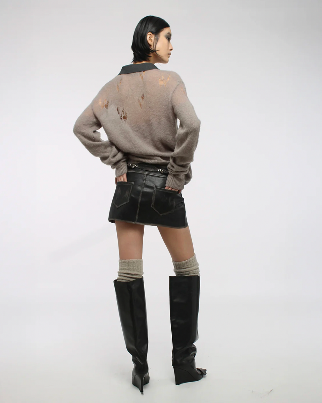 Person wearing a distressed sweater, black skirt, and knee-high boots on a white background