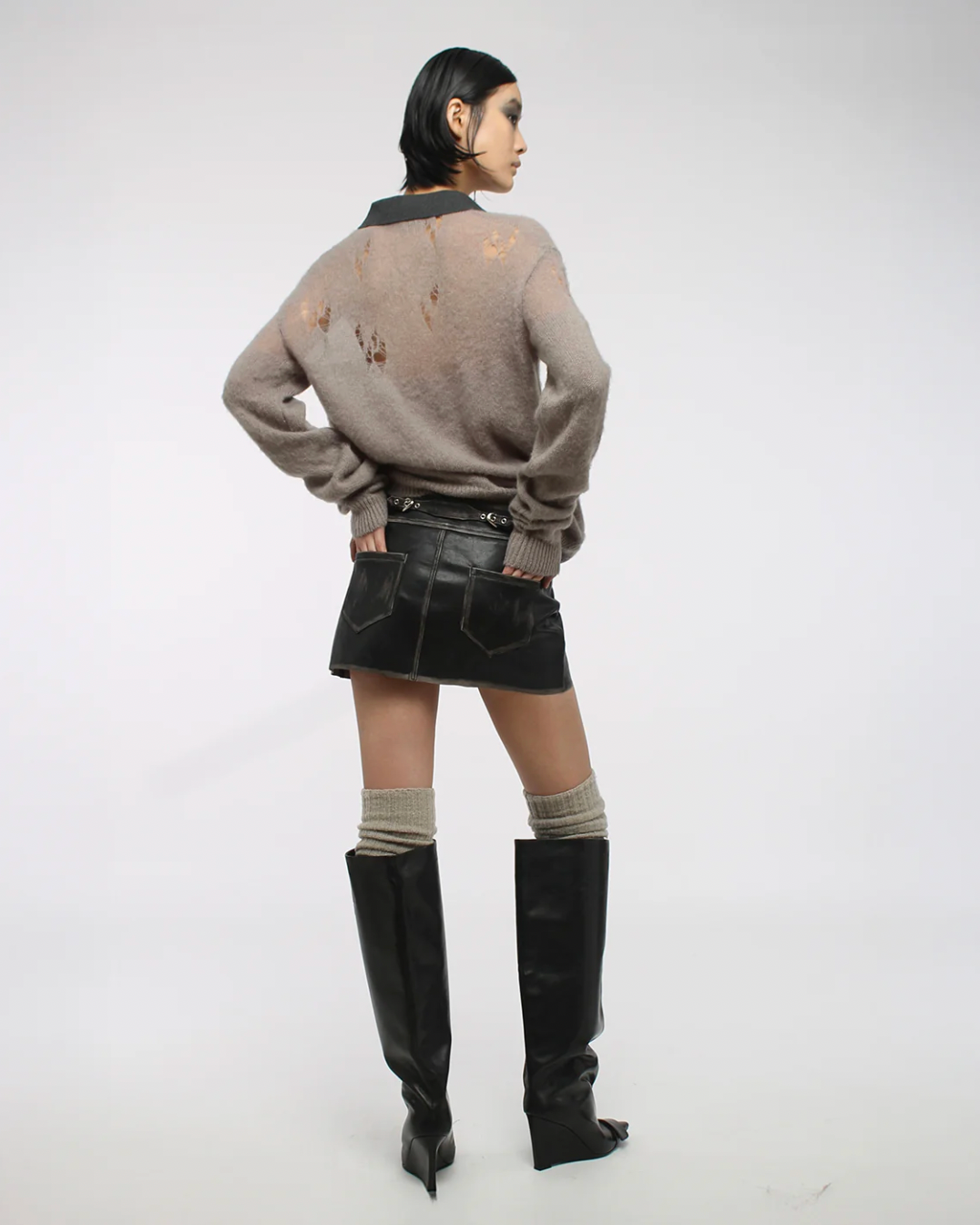 Person wearing a distressed sweater, black skirt, and knee-high boots on a white background
